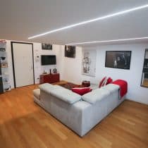 Accogliente soggiorno con pareti bianche, divano angolare e design moderno, luci a led e decorazioni artistiche.