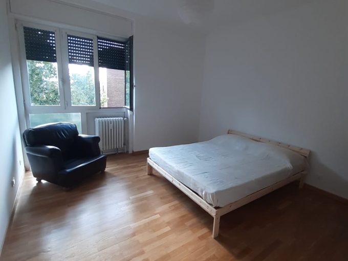 Ampia camera da letto arredata con letto e poltrona in soggiorno, luce naturale, pavimento in legno.