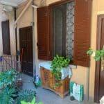 Finestra con persiana in legno su casa con piante verdi sul balcone.