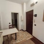 Ingresso di un appartamento con porta blindata, mobili e pareti bianche, pavimento in piastrelle di design, dettagli di arredamento e decorazioni.