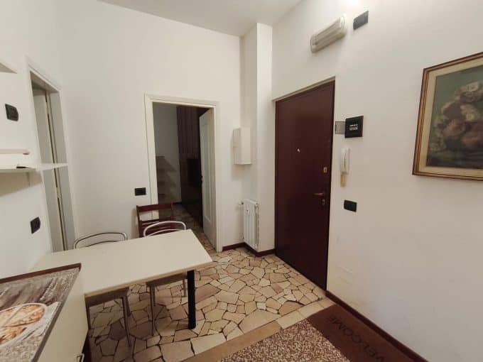 Ingresso di un appartamento con porta blindata, mobili e pareti bianche, pavimento in piastrelle di design, dettagli di arredamento e decorazioni.