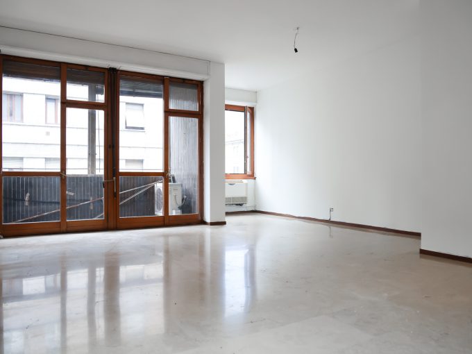 Ampio soggiorno con grandi finestre e balcone, luminoso e pronto per arredare.